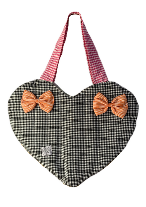 A heart-shaped fabric bag with a black and white gingham body, featuring two orange gingham bow accents on the front and pink-and-white gingham shoulder straps, shown against a plain white background.