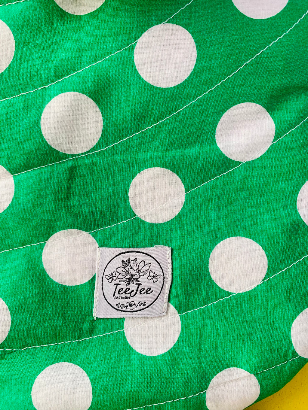 Close-up of a green fabric product with large white polka dots and a sewn-on label reading TeeJee Handmade.