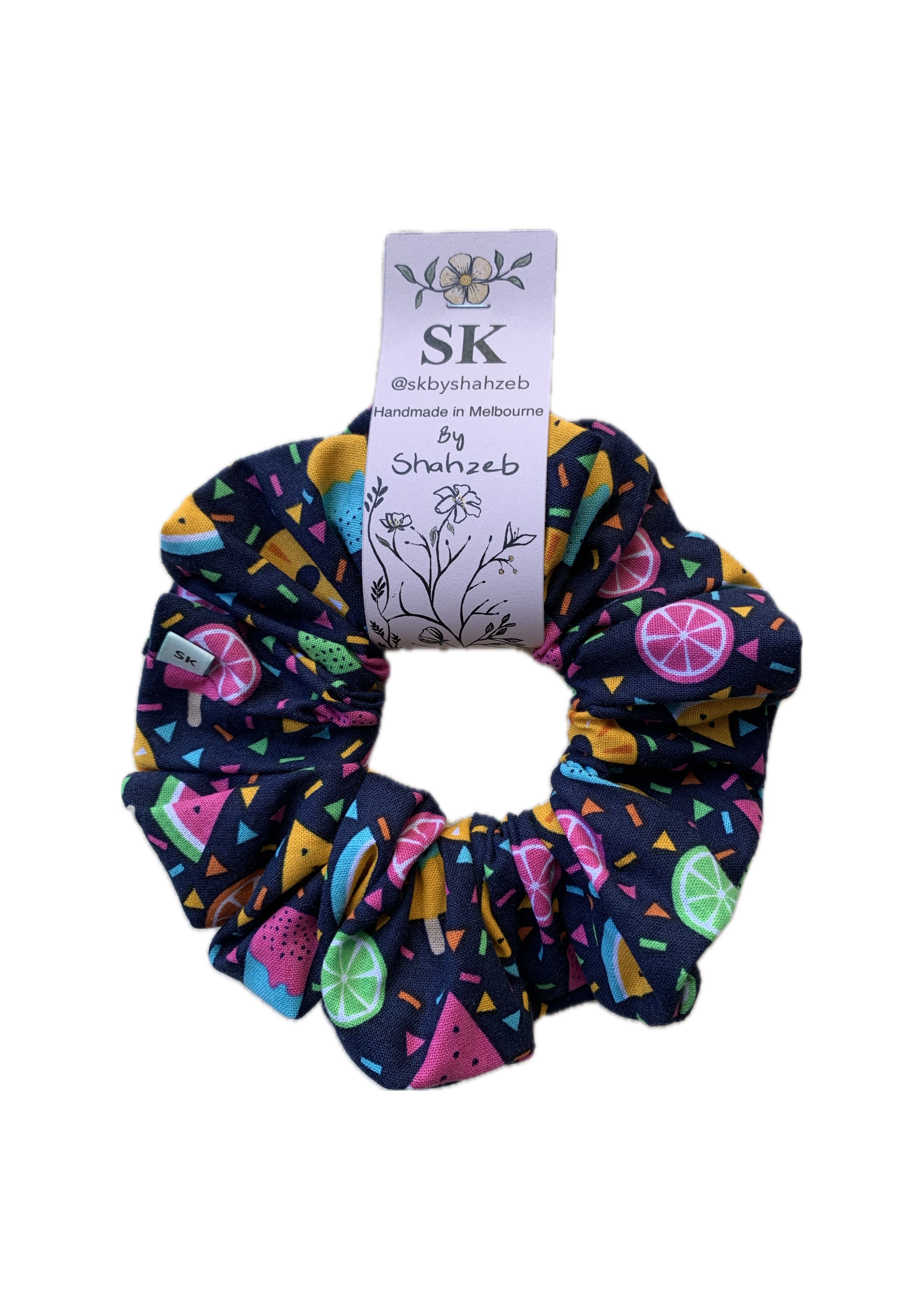 A fabric scrunchie with a colorful citrus and geometric pattern on a dark navy background.