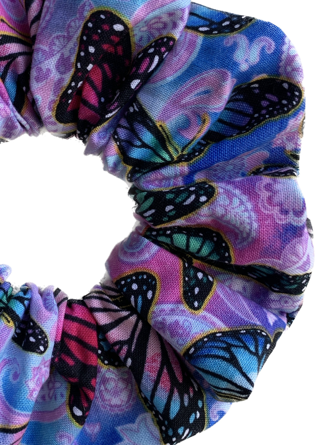 A close-up of a fabric hair scrunchie featuring a vibrant butterfly print on a purple, pink, and blue paisley background.