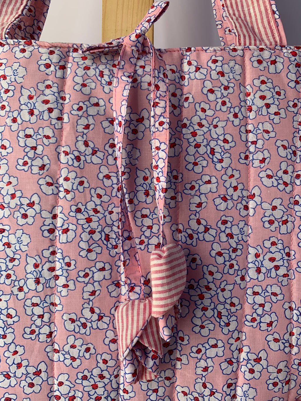 Pink floral tote bag with white and red flowers, featuring a tie closure and striped fabric handles.