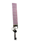 A pink and white patterned fabric keychain with a silver metal clasp and a key attached, shown against a plain white background.
