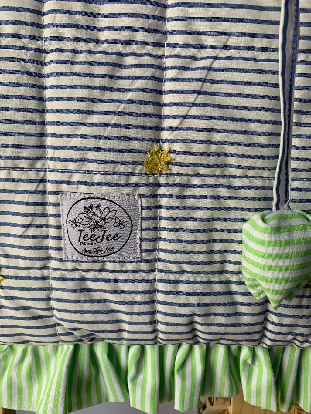 Close up of quilted tote bag with a gray and white striped pattern, and light green ruffled trim.