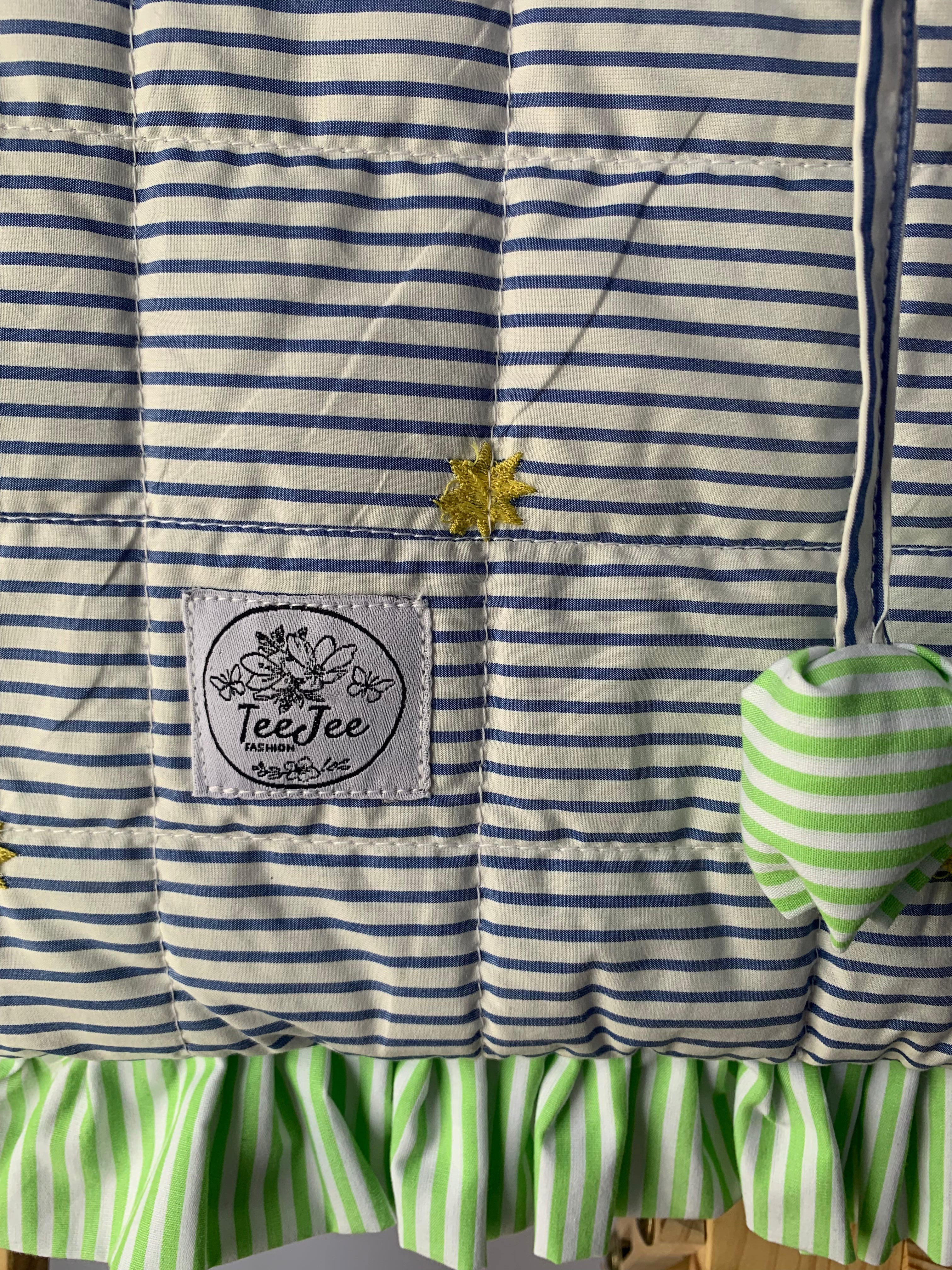 Close up of quilted tote bag with a gray and white striped pattern, and light green ruffled trim.