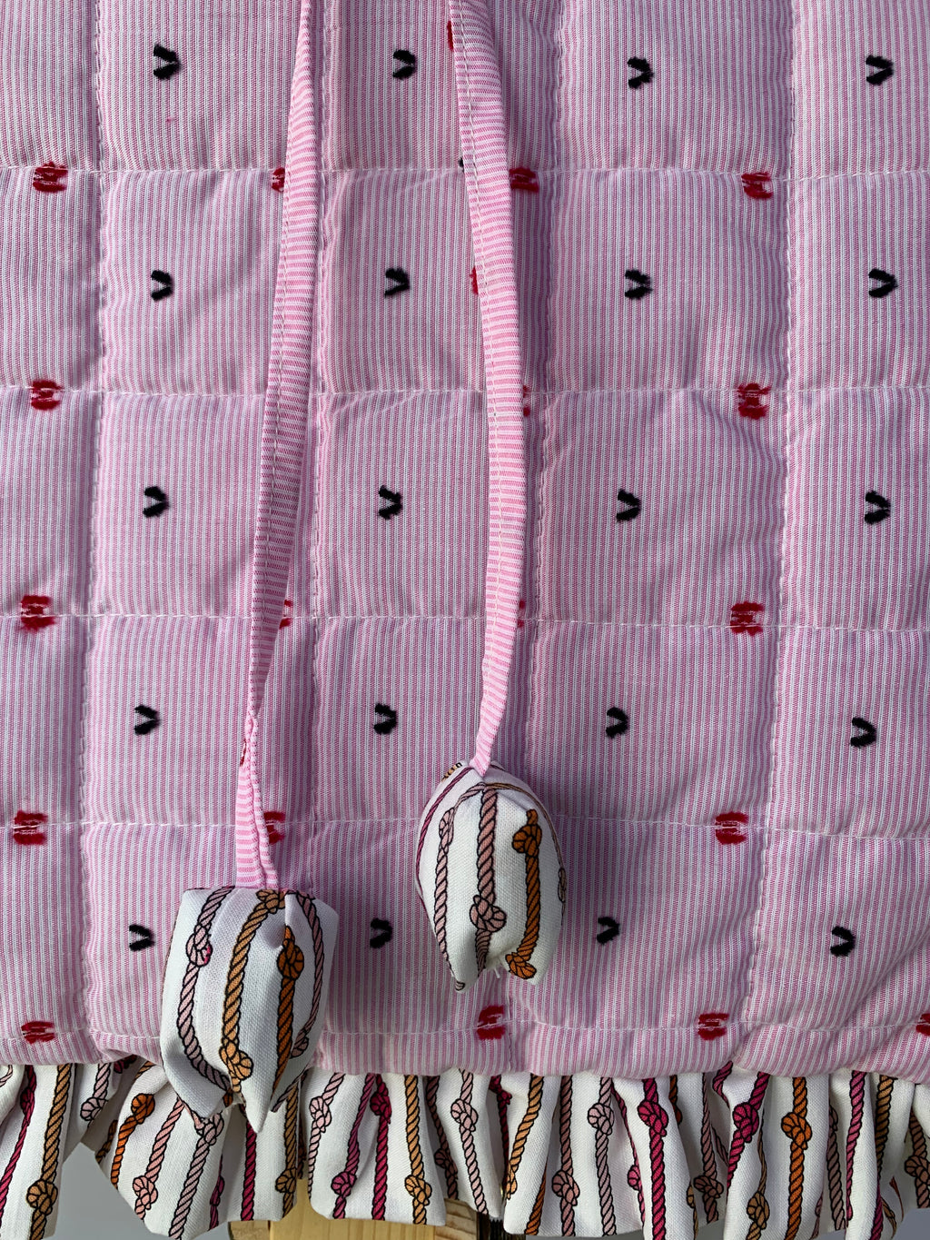 A close-up of a quilted tote bag, a pink drawstring, and a ruffled hem with a western-style rope print.