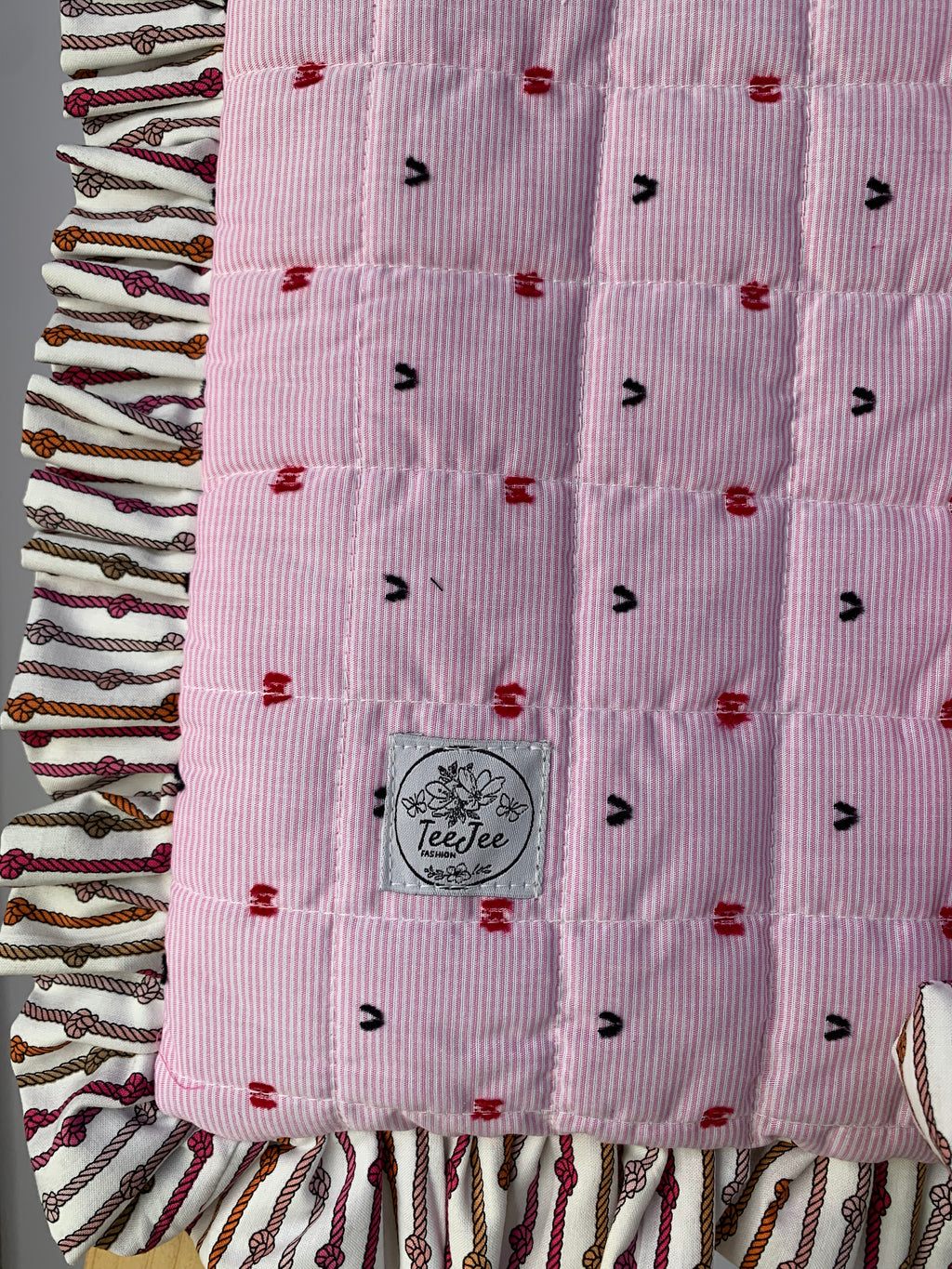 A close-up of a quilted pink tote with small embroidered motifs, ruffled edges, and a visible sewn-on label reading TeeJee.