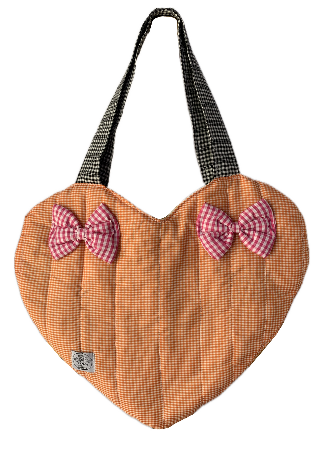 A heart-shaped quilted fabric bag in a small orange and white gingham pattern, featuring two pink and white gingham bow accents on the front and black-and-white gingham shoulder straps.