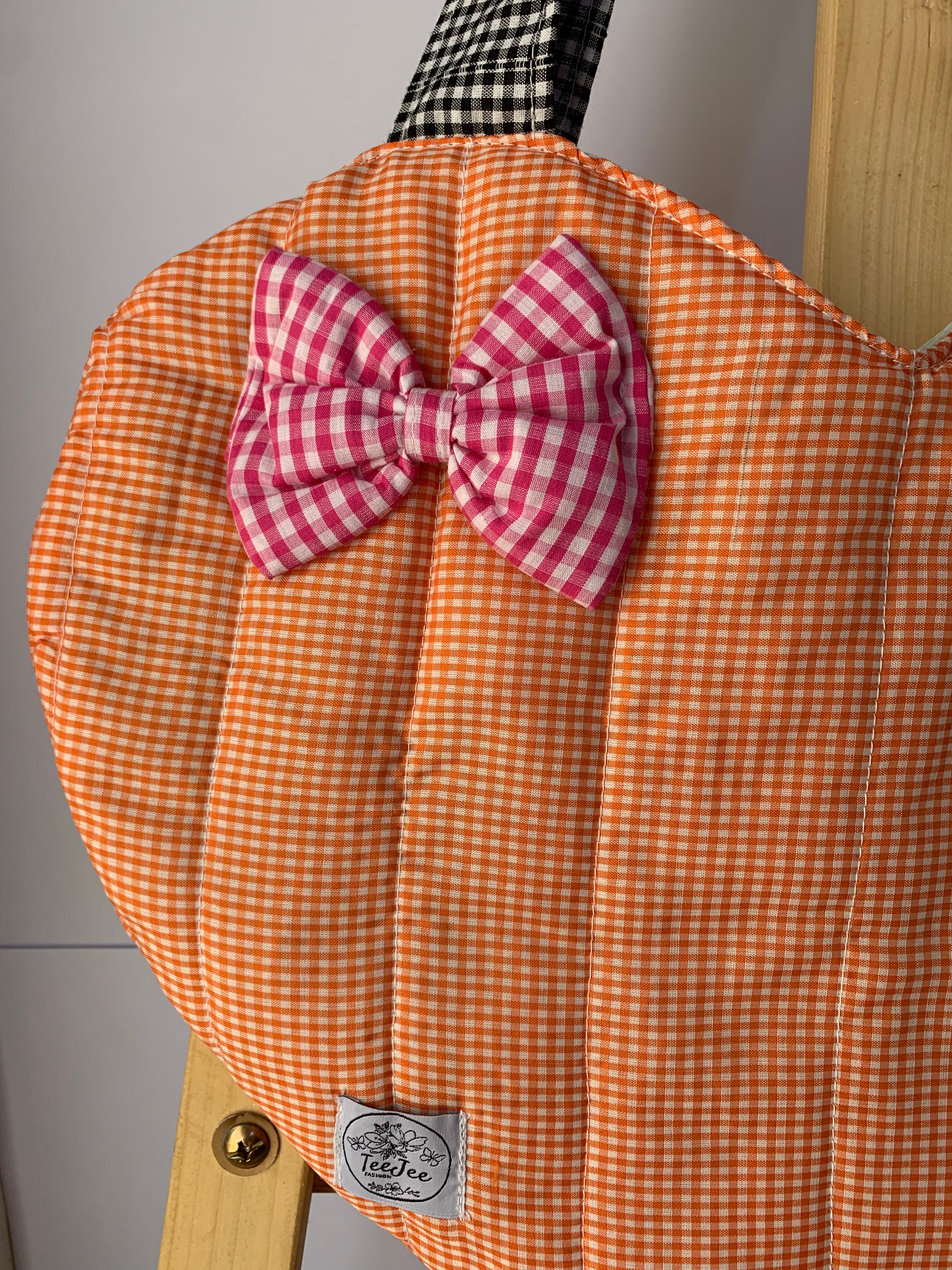 An orange and white gingham quilted tote bag with a matching pink and white gingham bow on the front.