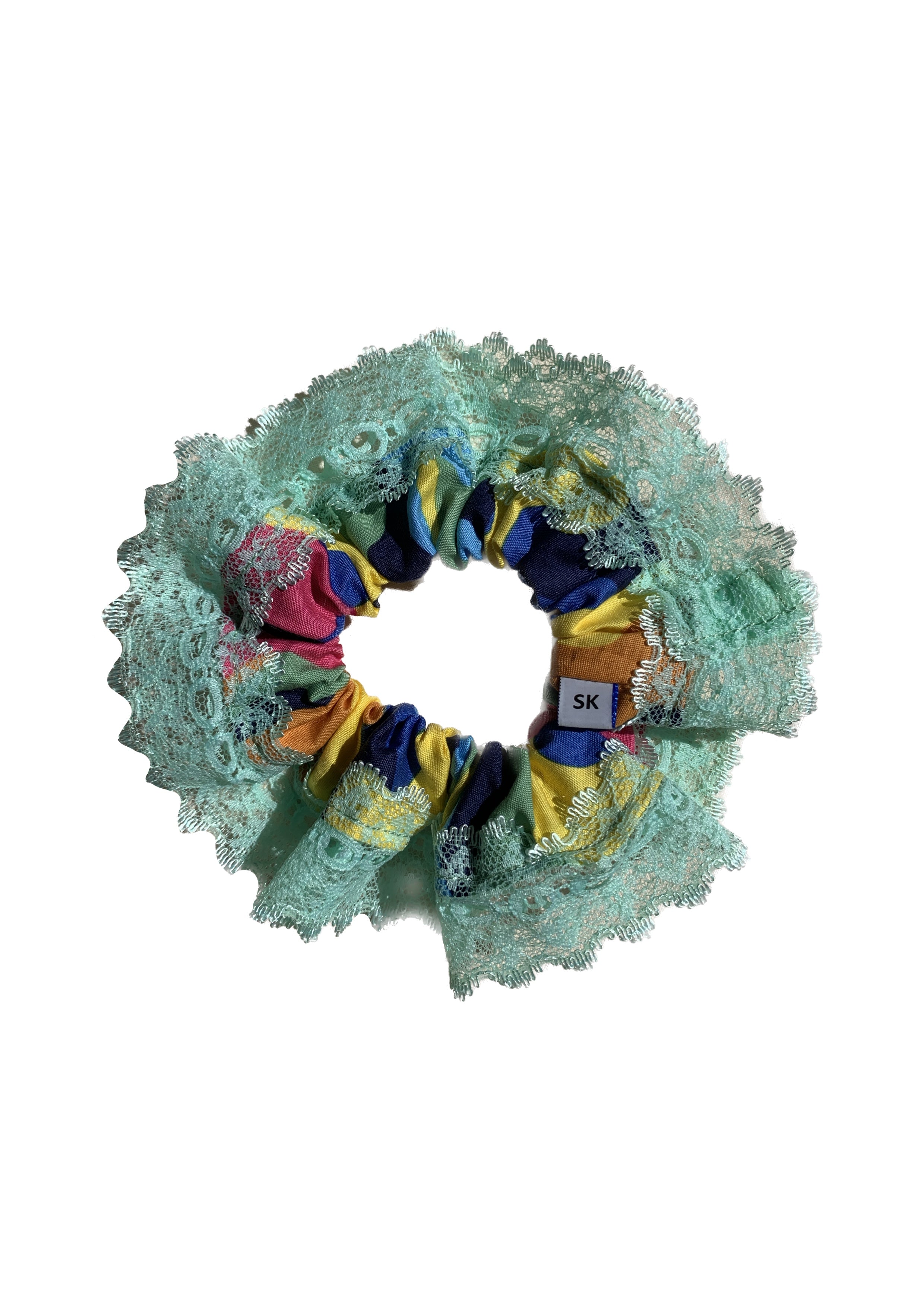 A handmade fabric scrunchie featuring a mint green lace ruffle outer layer and a colorful inner layer with yellow, blue, pink, and orange patterned fabric.