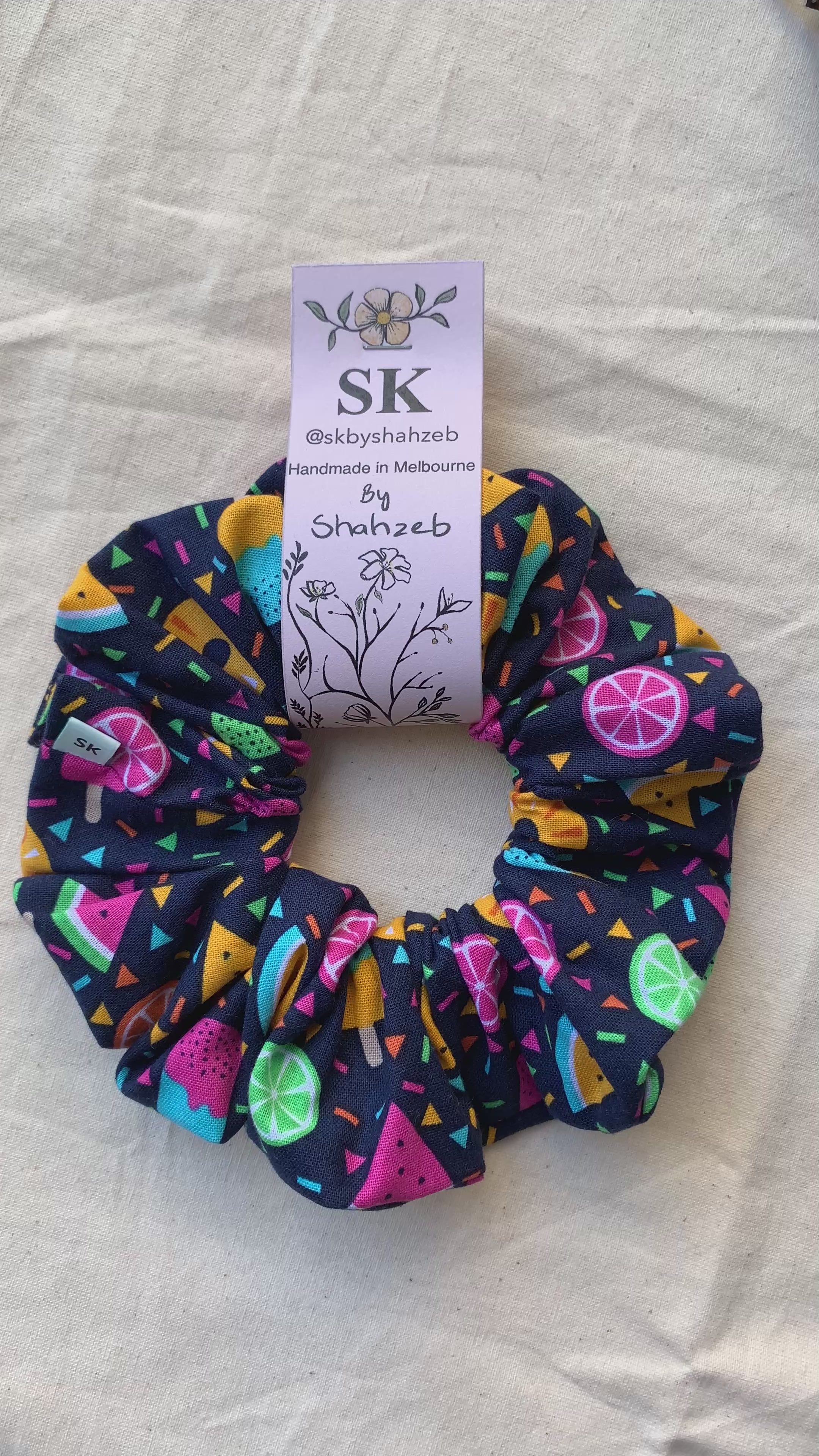 A fabric scrunchie with a colorful citrus and geometric pattern on a dark navy background.