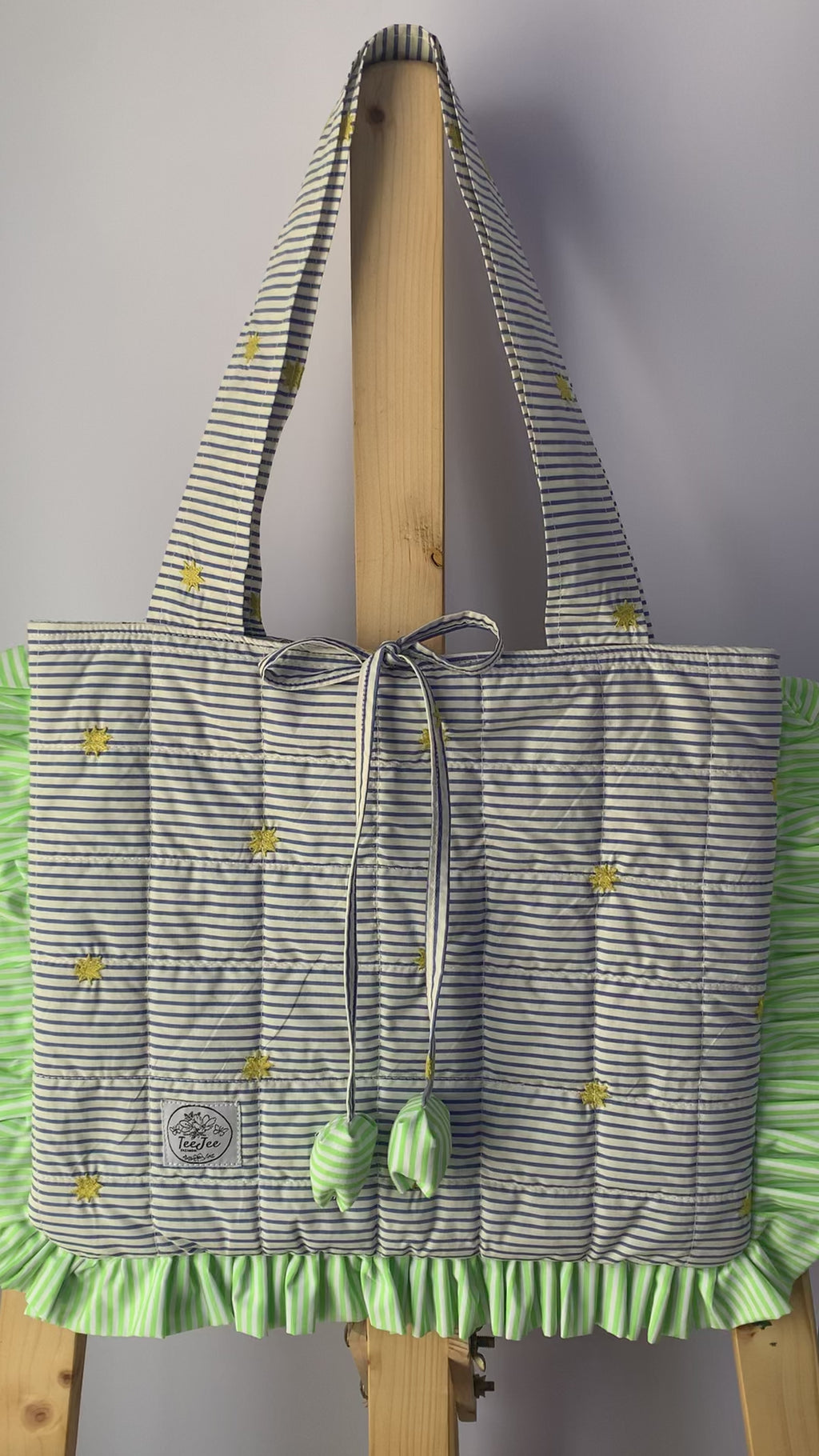 A video showing quilted tote bag with a gray and white striped pattern, and light green ruffled trim.