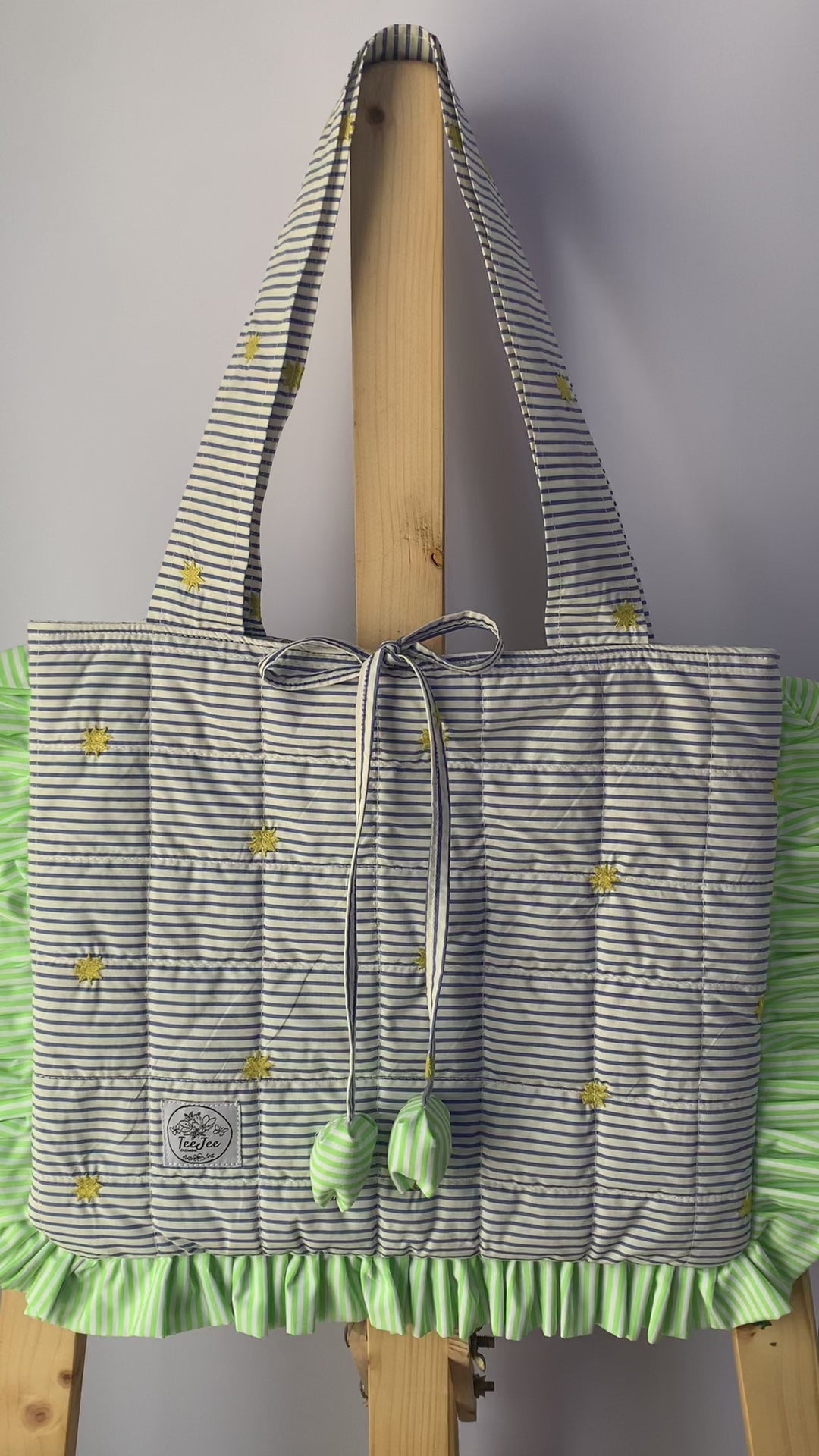 A video showing quilted tote bag with a gray and white striped pattern, and light green ruffled trim.
