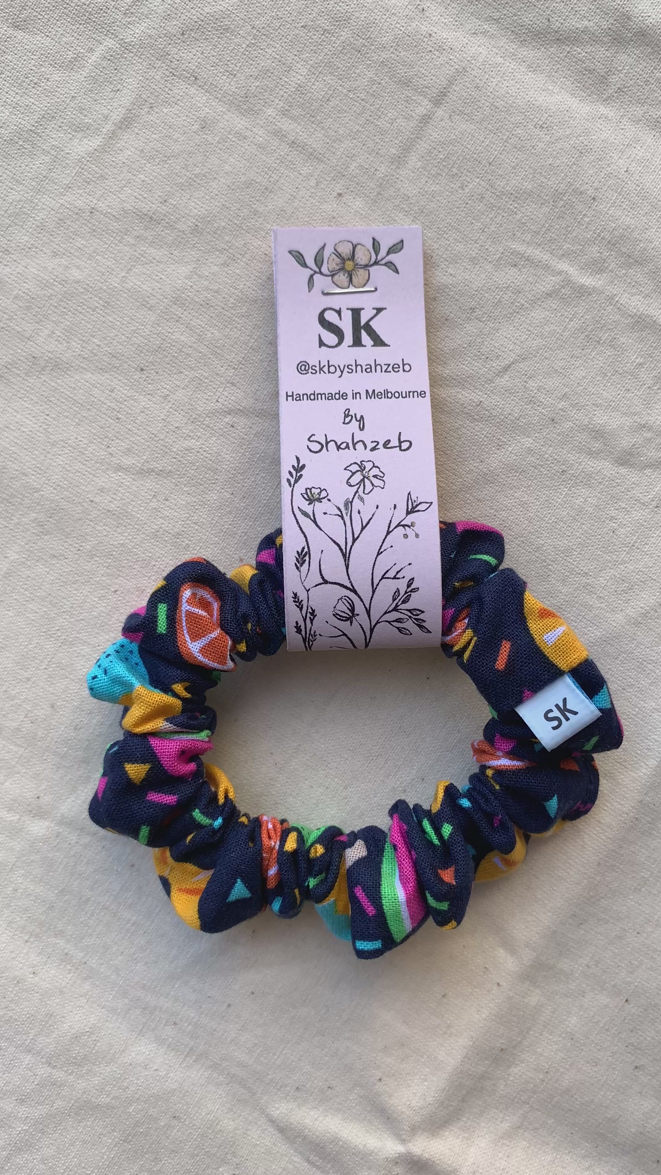 A fabric scrunchie with a colorful citrus and geometric pattern on a dark navy background.