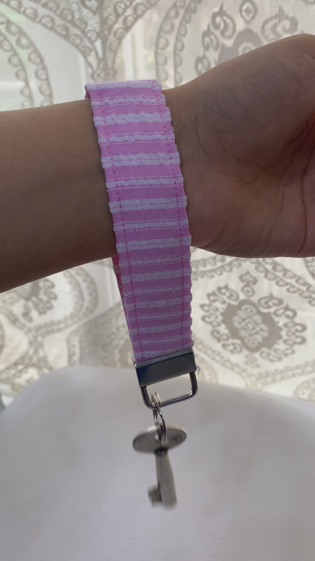 A video showing pink and white patterned fabric keychain with a silver metal clasp and a key attached, shown against a plain white background.